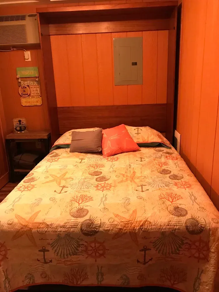 A bed with an orange wall behind it, a nightstand, and a blanket with a seashell pattern.