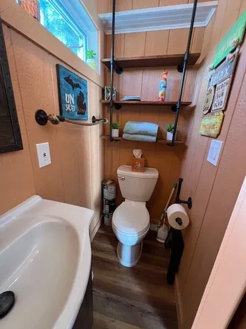 Small bathroom with toilet, sink, wooden shelves, and orange walls.