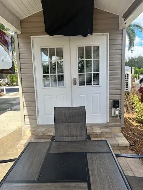 Outdoor patio with table and chair in front of white double doors with a covered television mounted above.