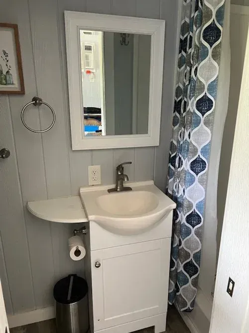Small bathroom with white vanity, mirror, blue patterned shower curtain, and toilet paper roll.