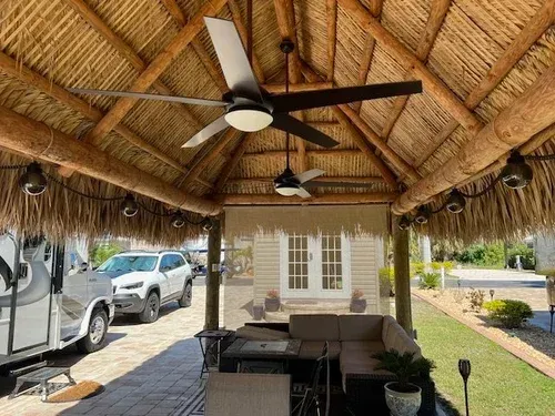 Thatched roof outdoor living space with fans, seating, and vehicles.