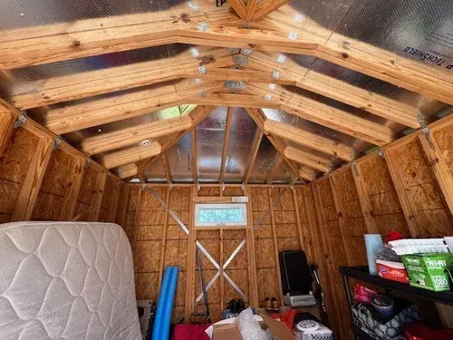 Interior view of a wooden shed with a mattress, shelves, and a small window at the back.