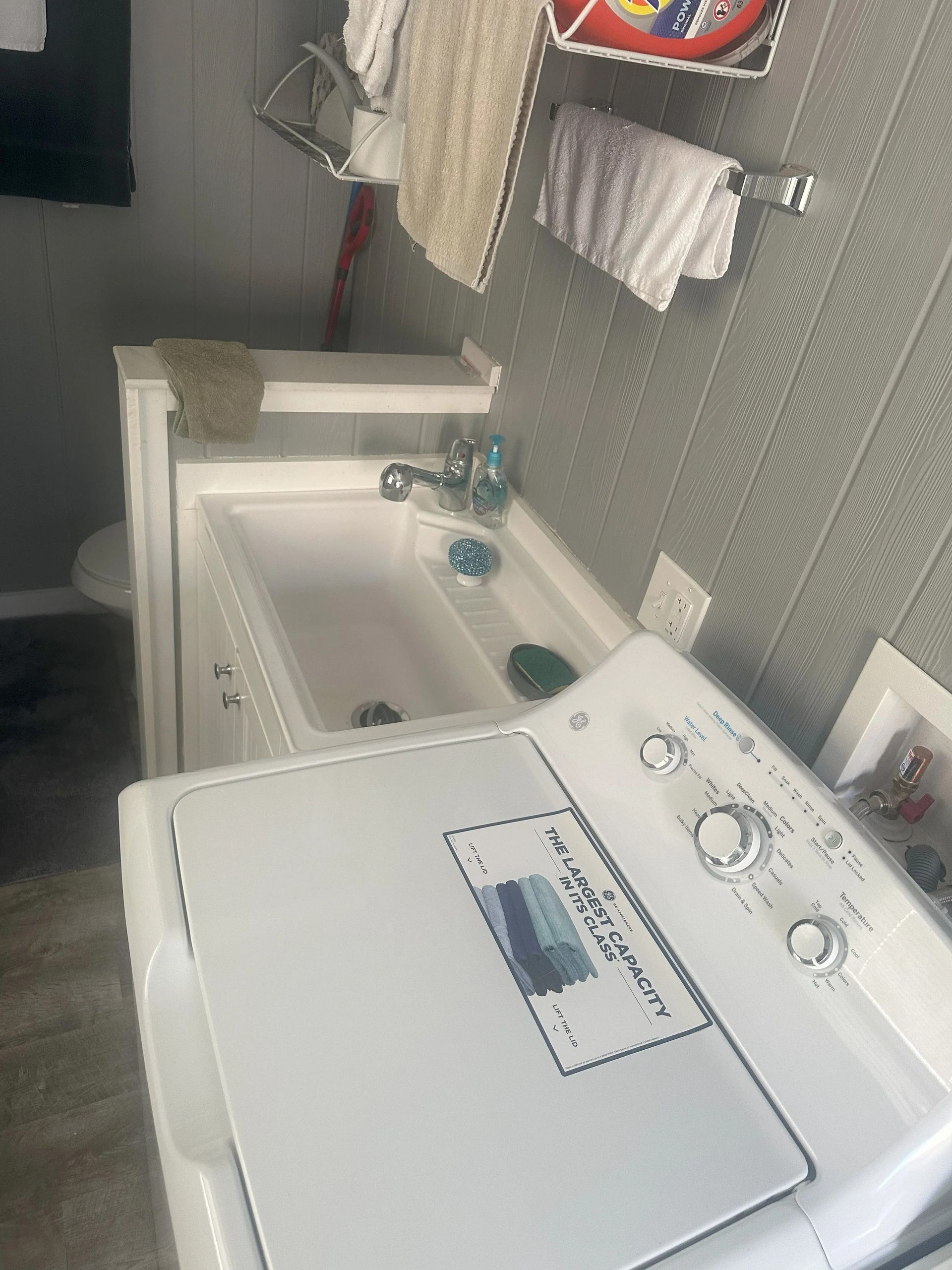 A laundry room with a washing machine and sink, towels hanging on a wall, and a toilet.