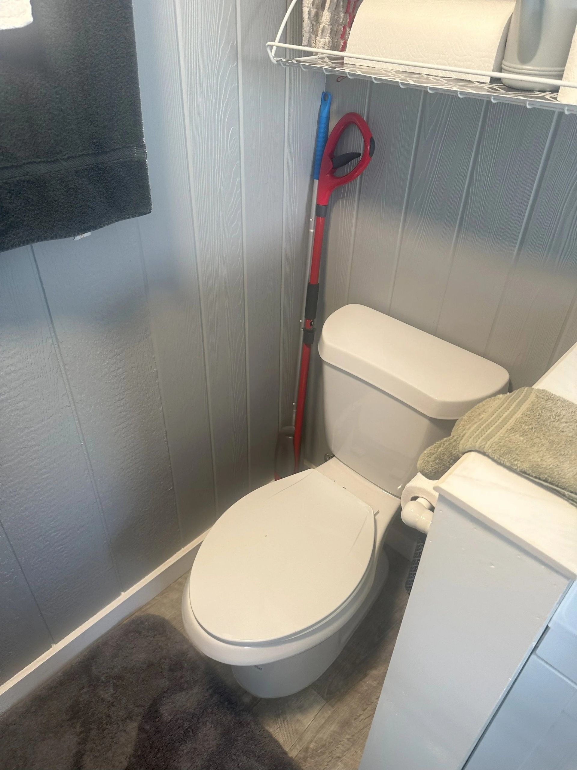 Toilet in a small bathroom with a mop leaning against the wall.
