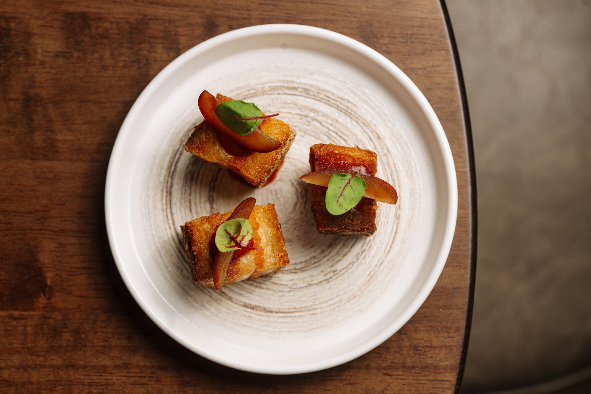 A white plate topped with three pieces of food on a wooden table.