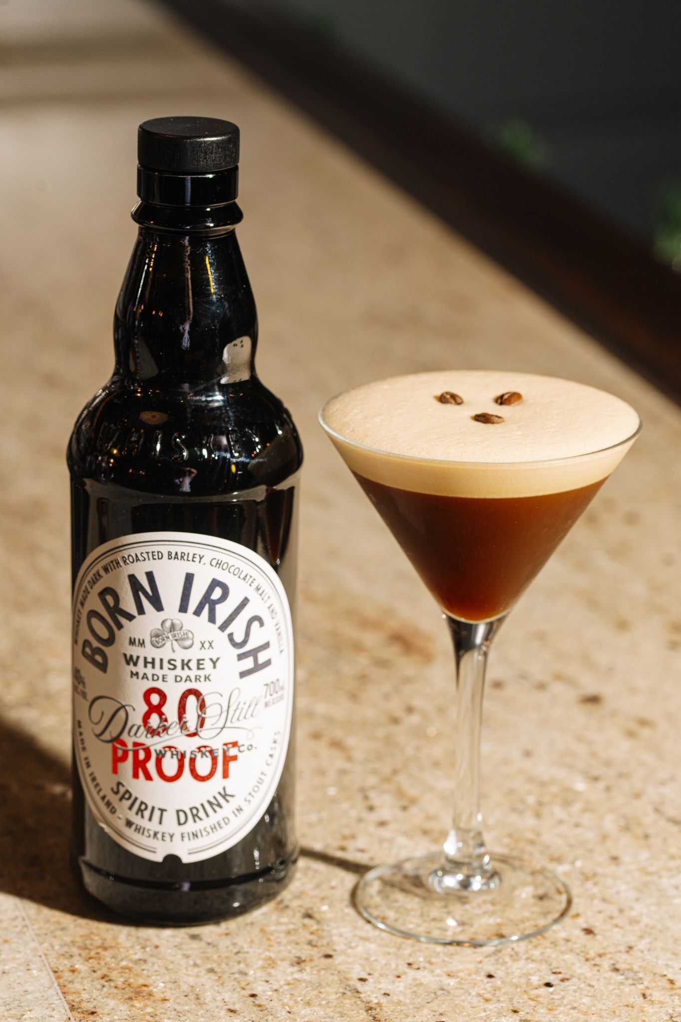 A bottle of corn irish whiskey next to a martini glass on a counter.