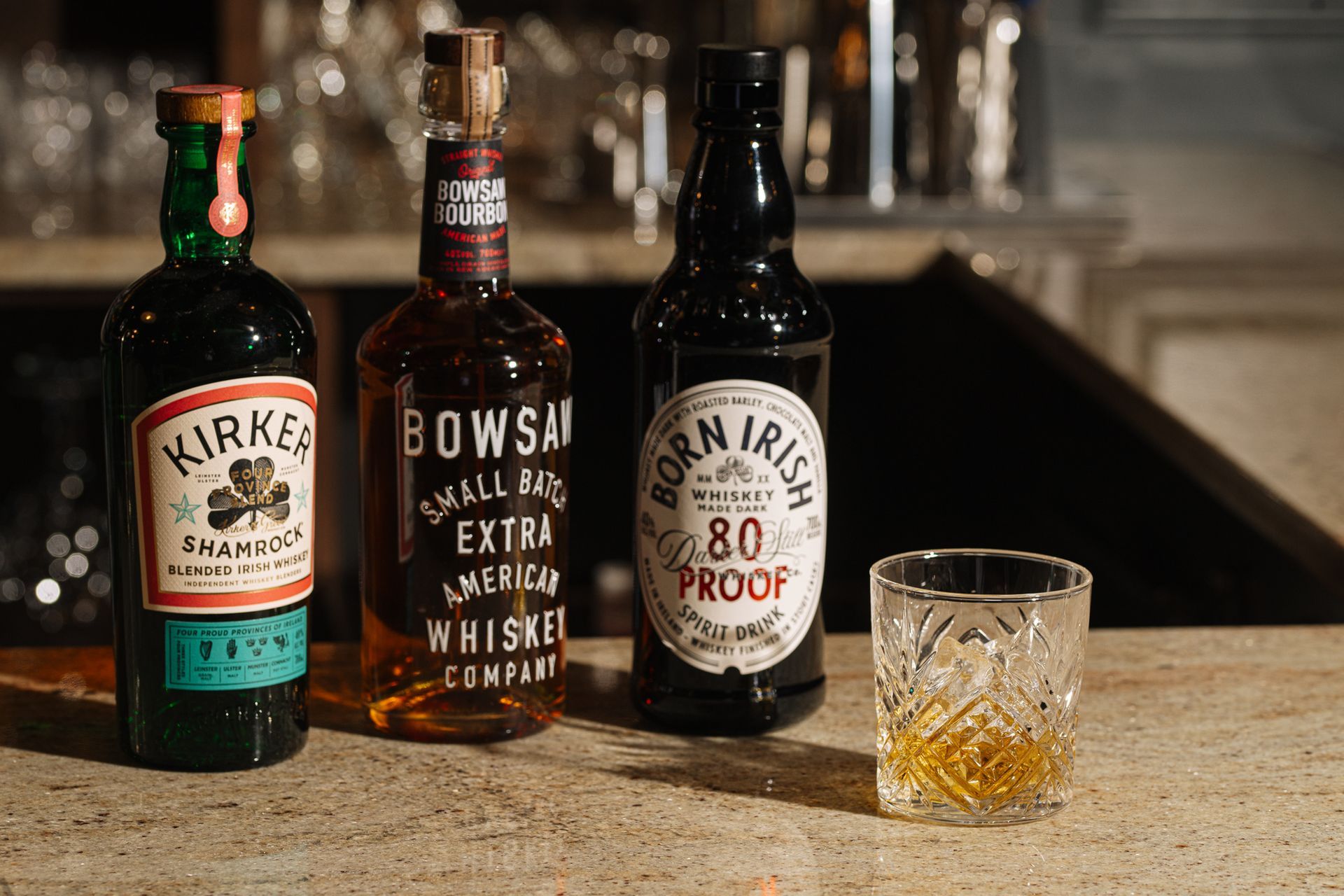 Three bottles of whiskey and a glass of whiskey are sitting on a counter.