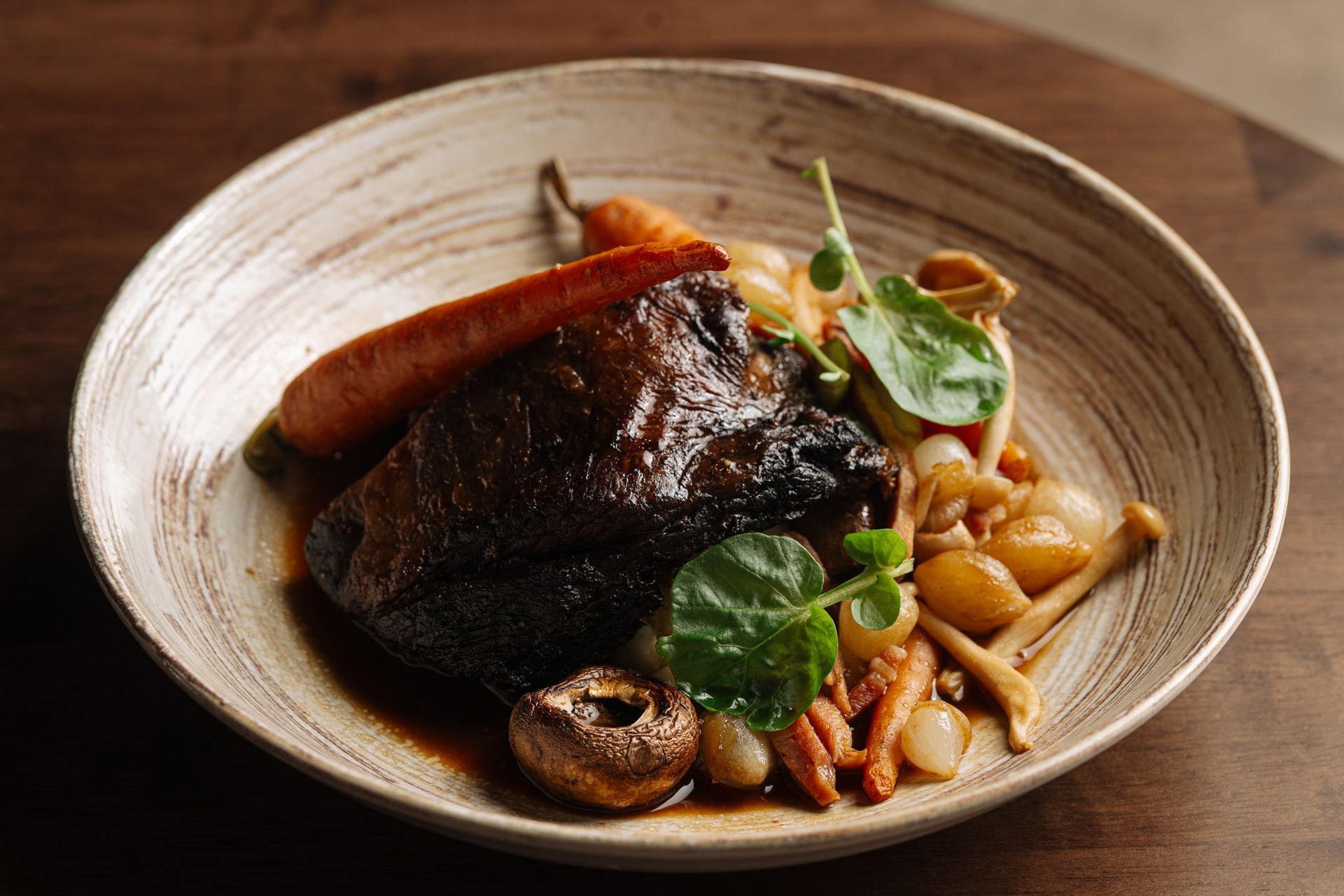 A plate of food with meat , carrots , mushrooms and beans on a wooden table.