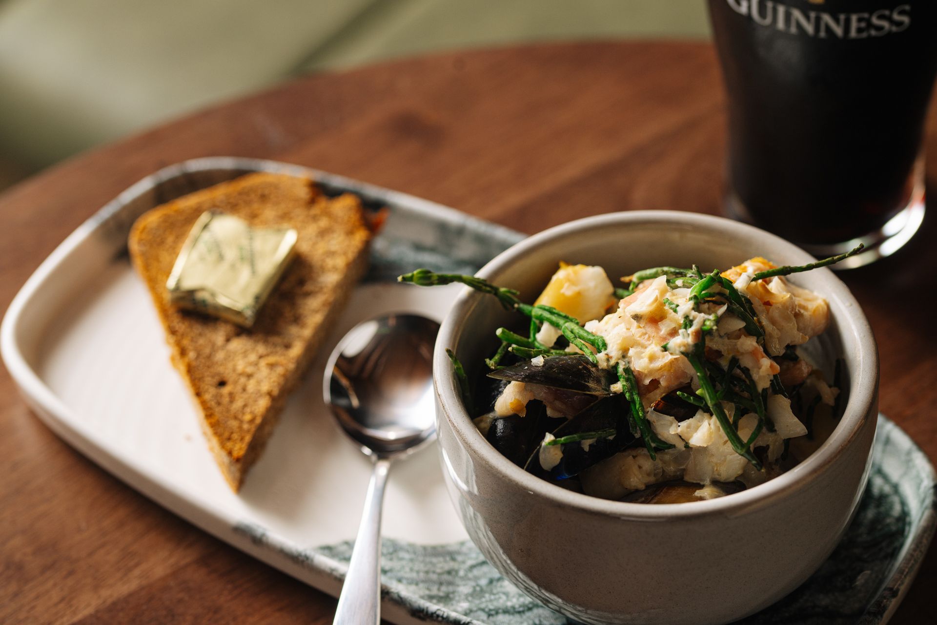 A bowl of soup with a spoon and a piece of bread on a plate.