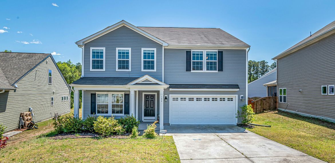 Two-story blue house with a white garage door and a green lawn under a blue sky.