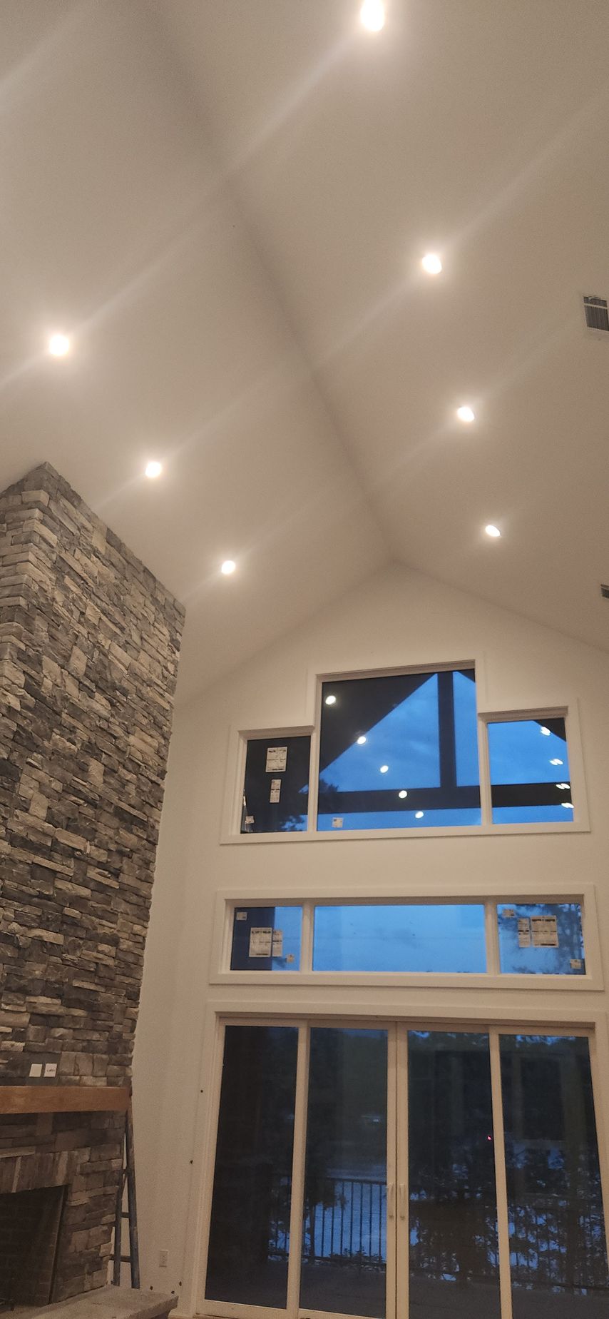 Interior of a home with a tall ceiling, recessed lighting, stone fireplace, and large windows.