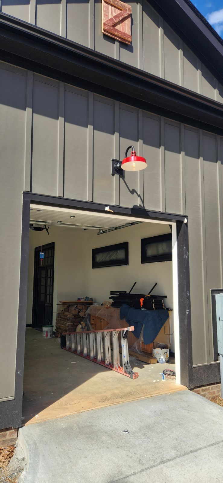 A gray building with an open garage door and a red and white light fixture above it.
