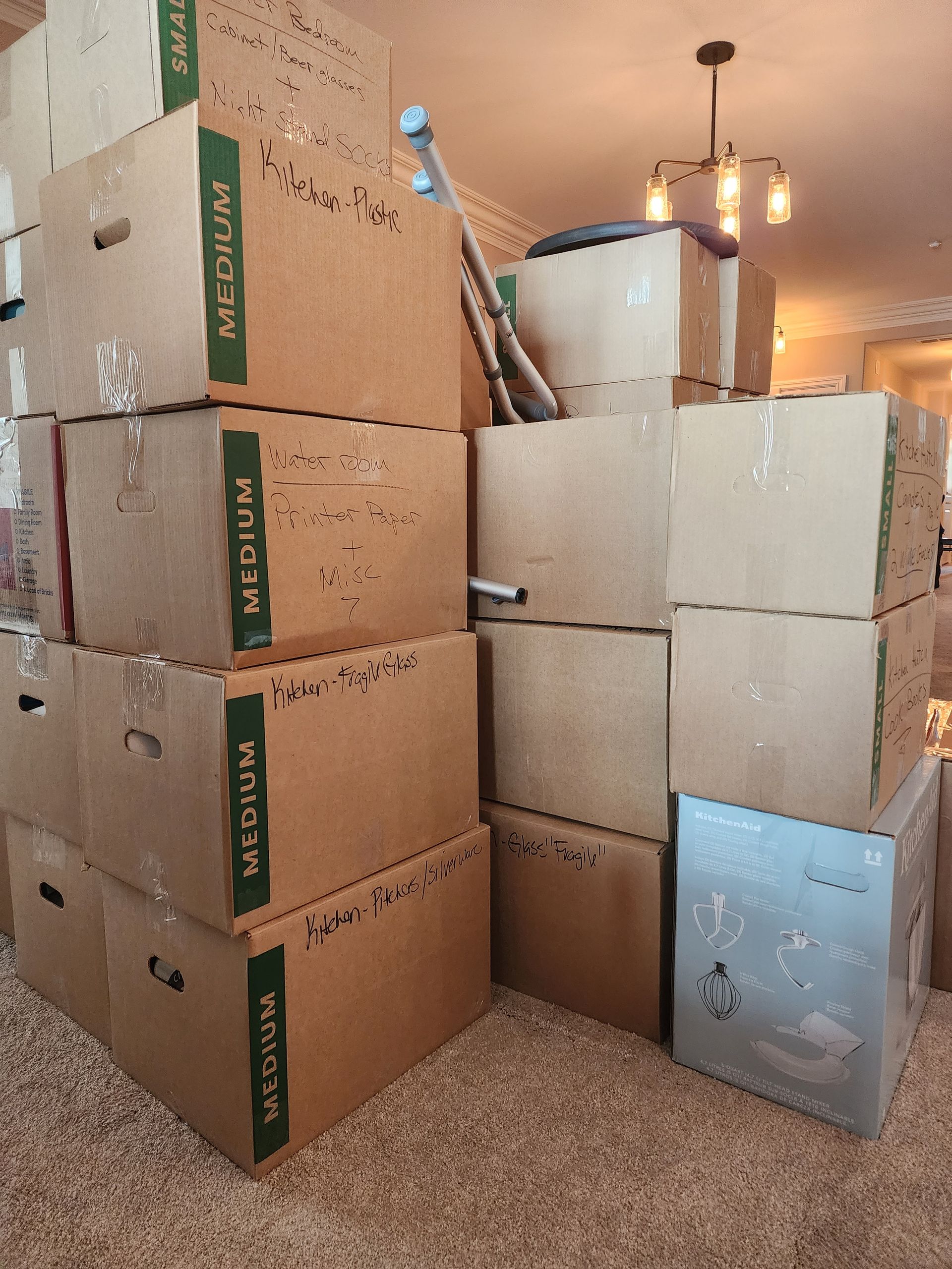 Piles of cardboard boxes stacked in a room, indicating a move. Some boxes are labeled 