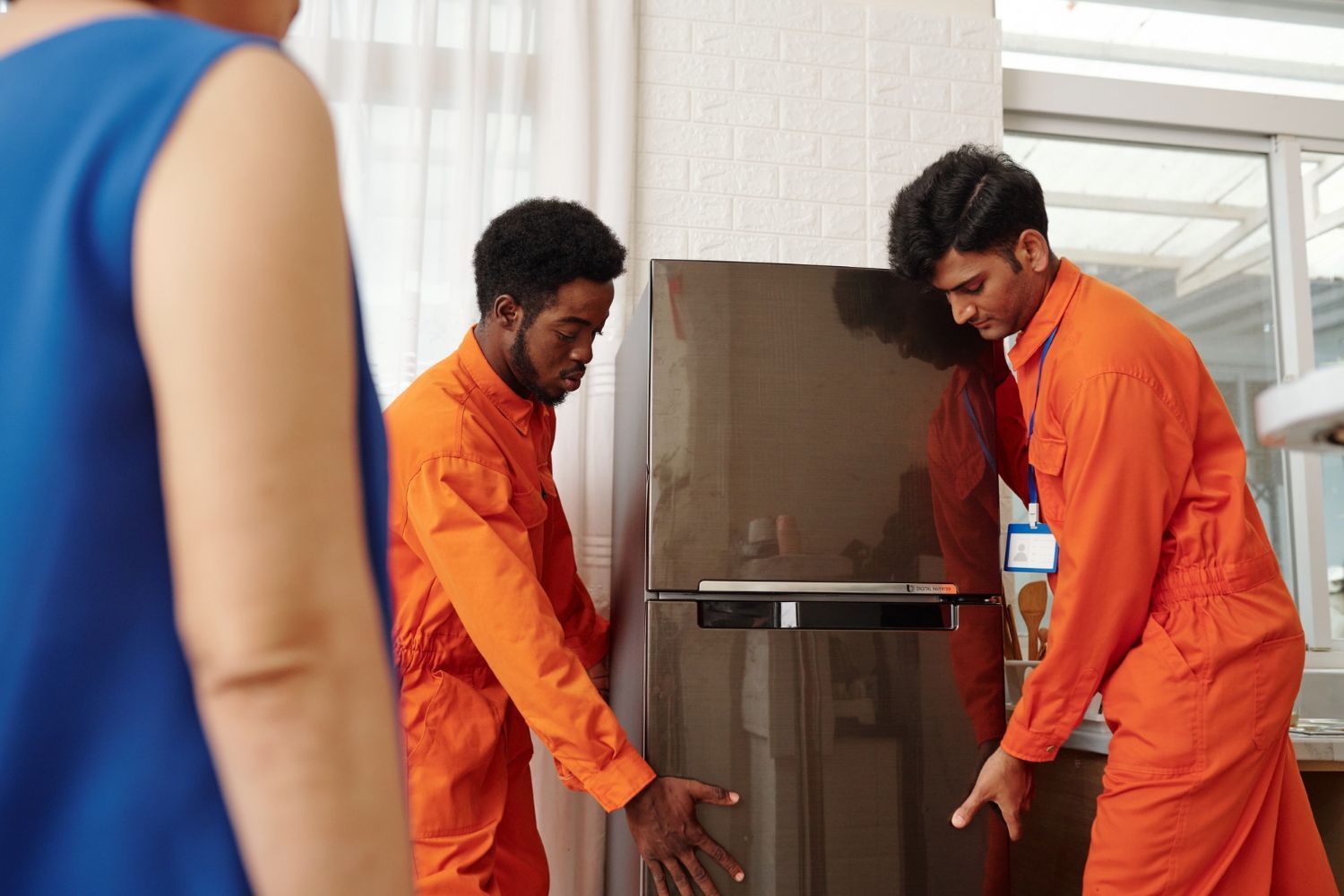 Two men in orange jumpsuits are moving a refrigerator.