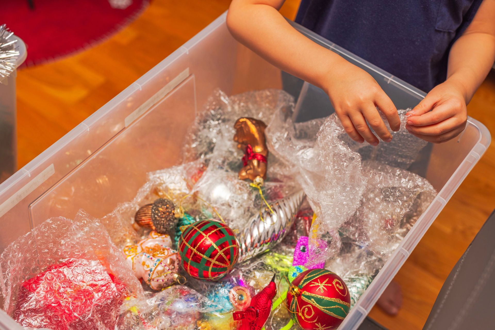 Child packing Christmas ornaments in a plastic bin filled with bubble wrap.