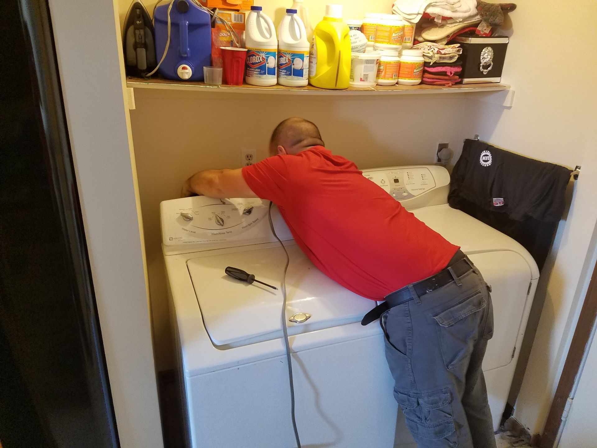 a man in a red shirt is working on a washer and dryer
