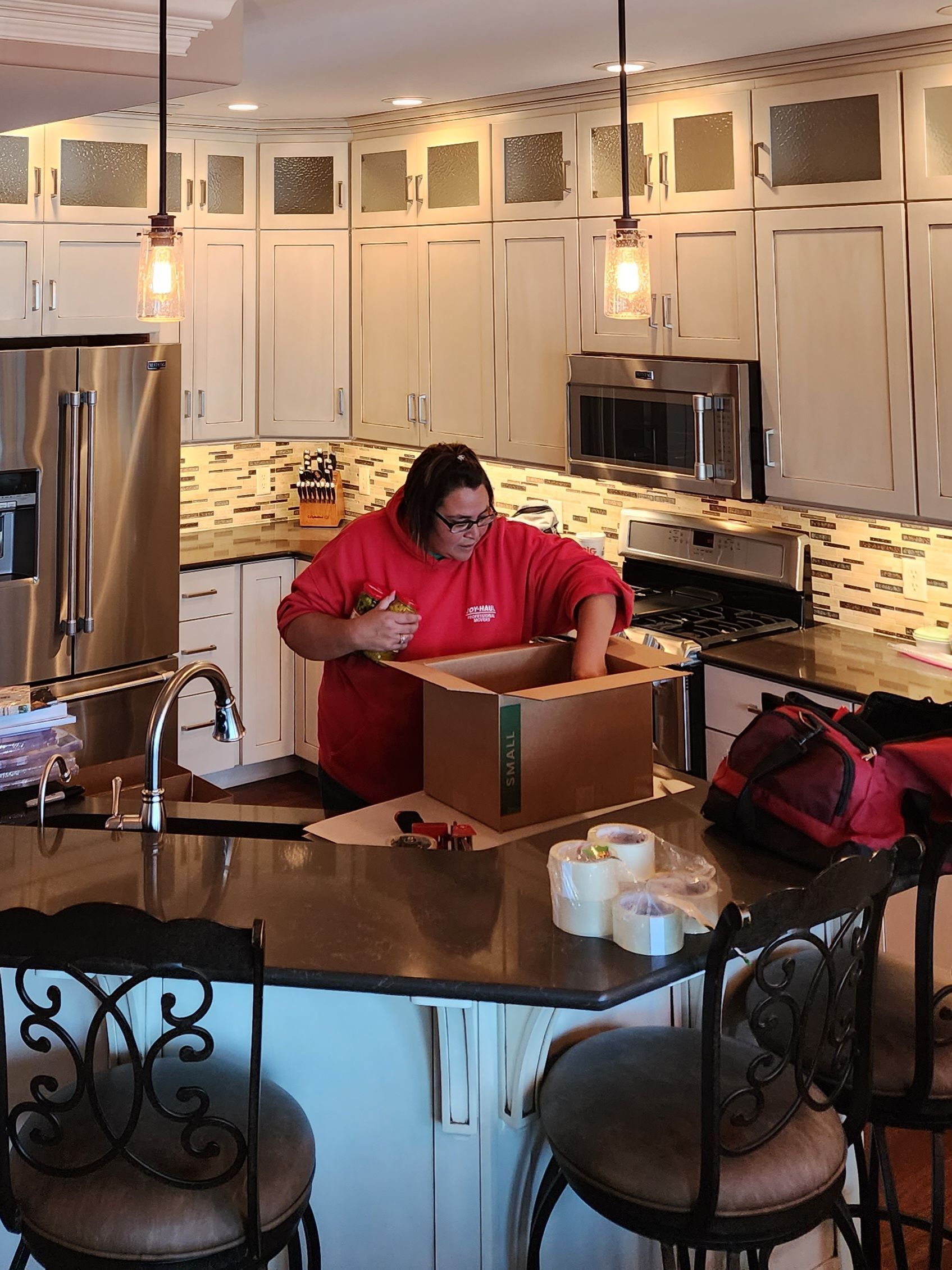 a woman in a red shirt is standing in a kitchen packing a box .