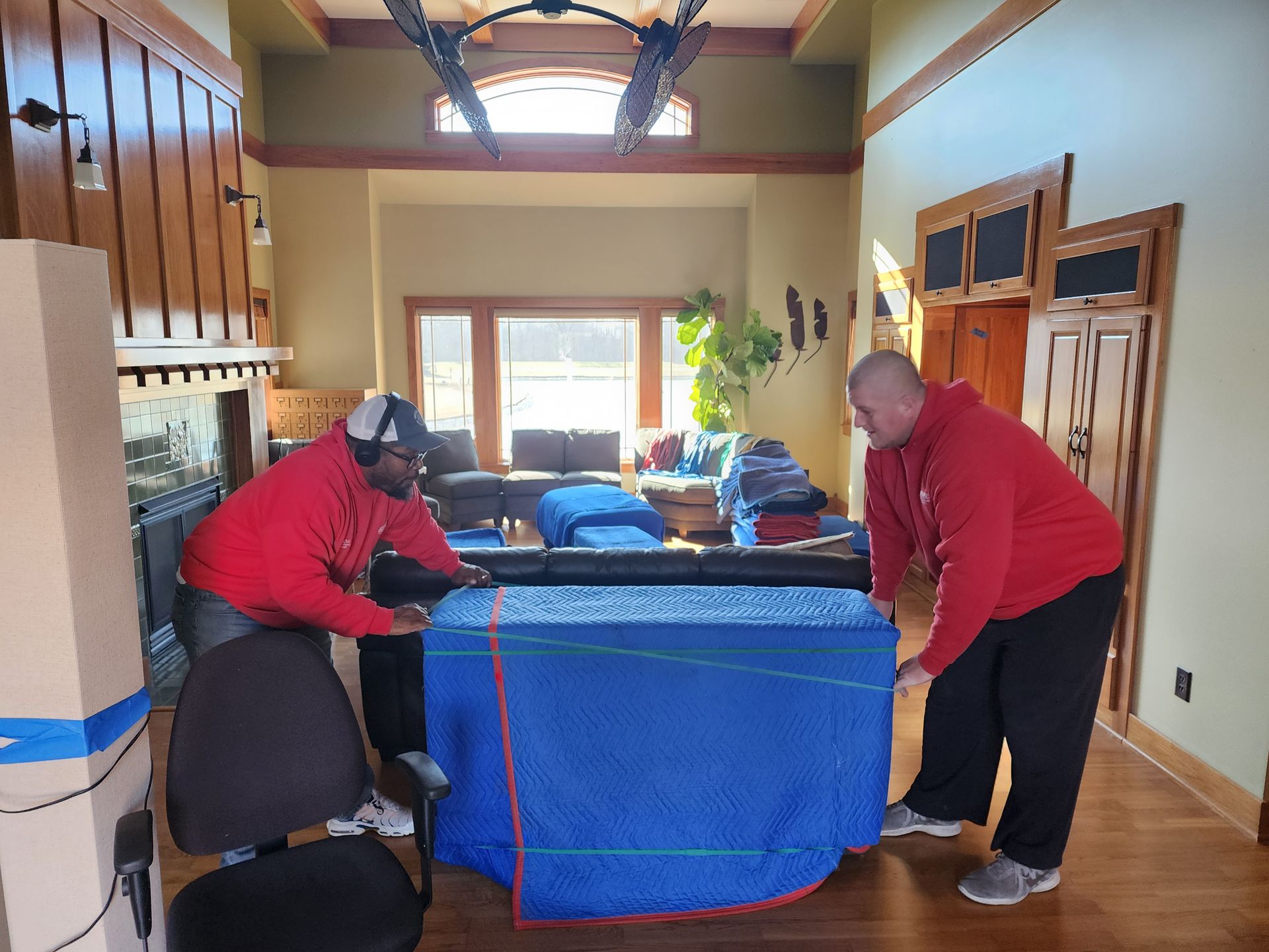 two men in red sweatshirts are moving a couch in a living room