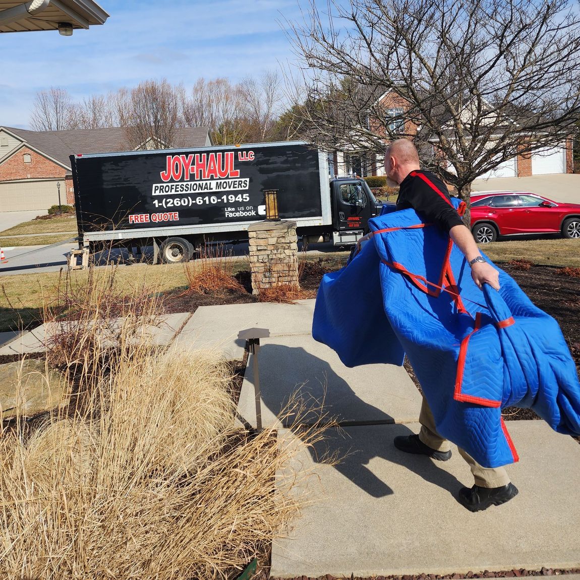 a man is carrying a blue blanket in front of a john 's moving truck