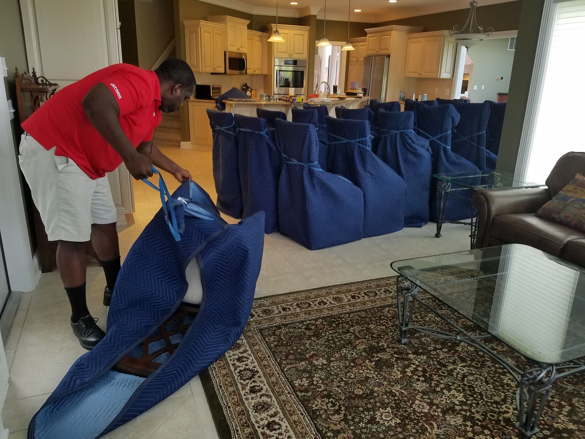 A man in a red shirt is holding a blue bag in a living room.