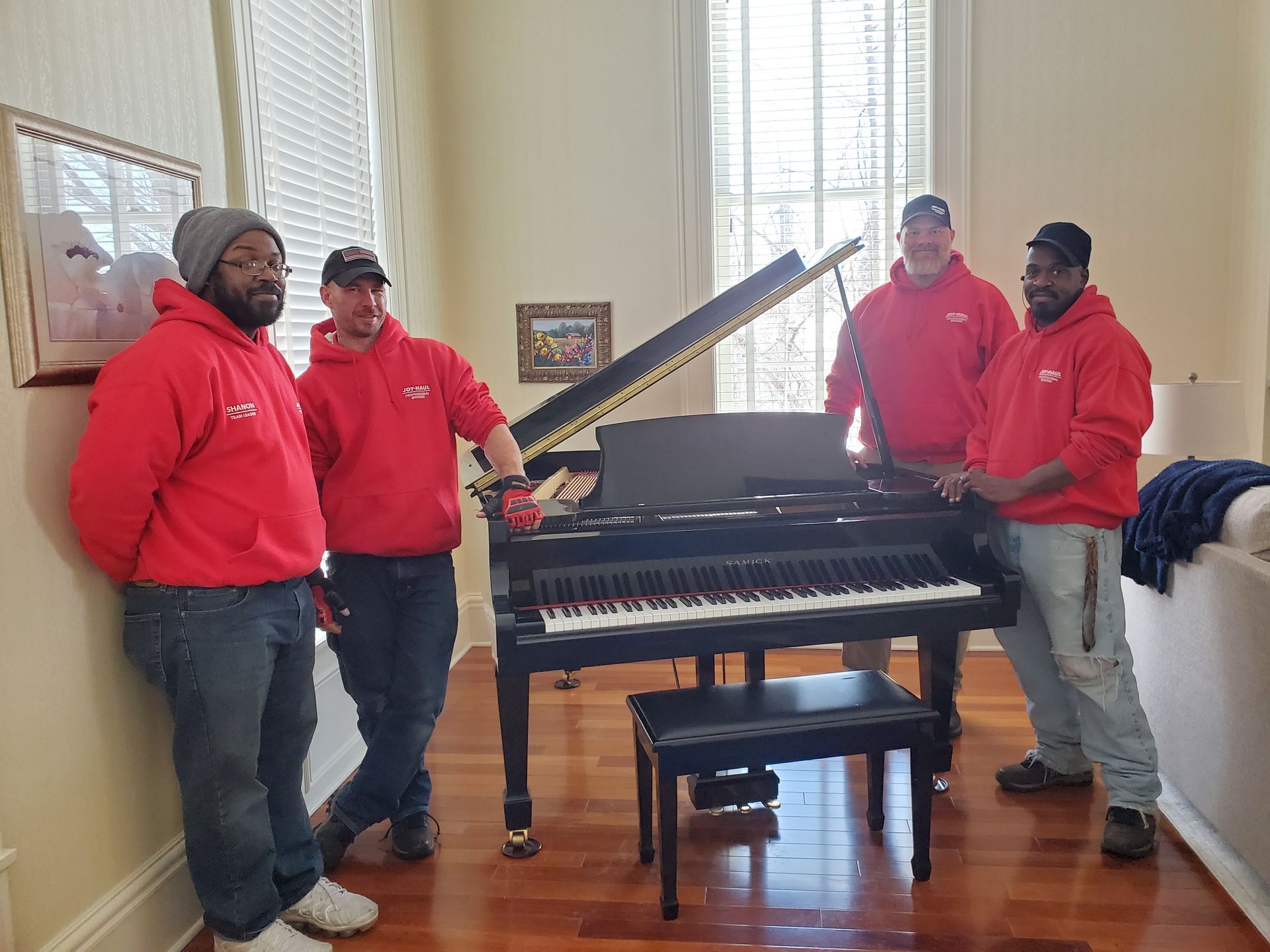 A group of men are standing next to a piano in a living room.