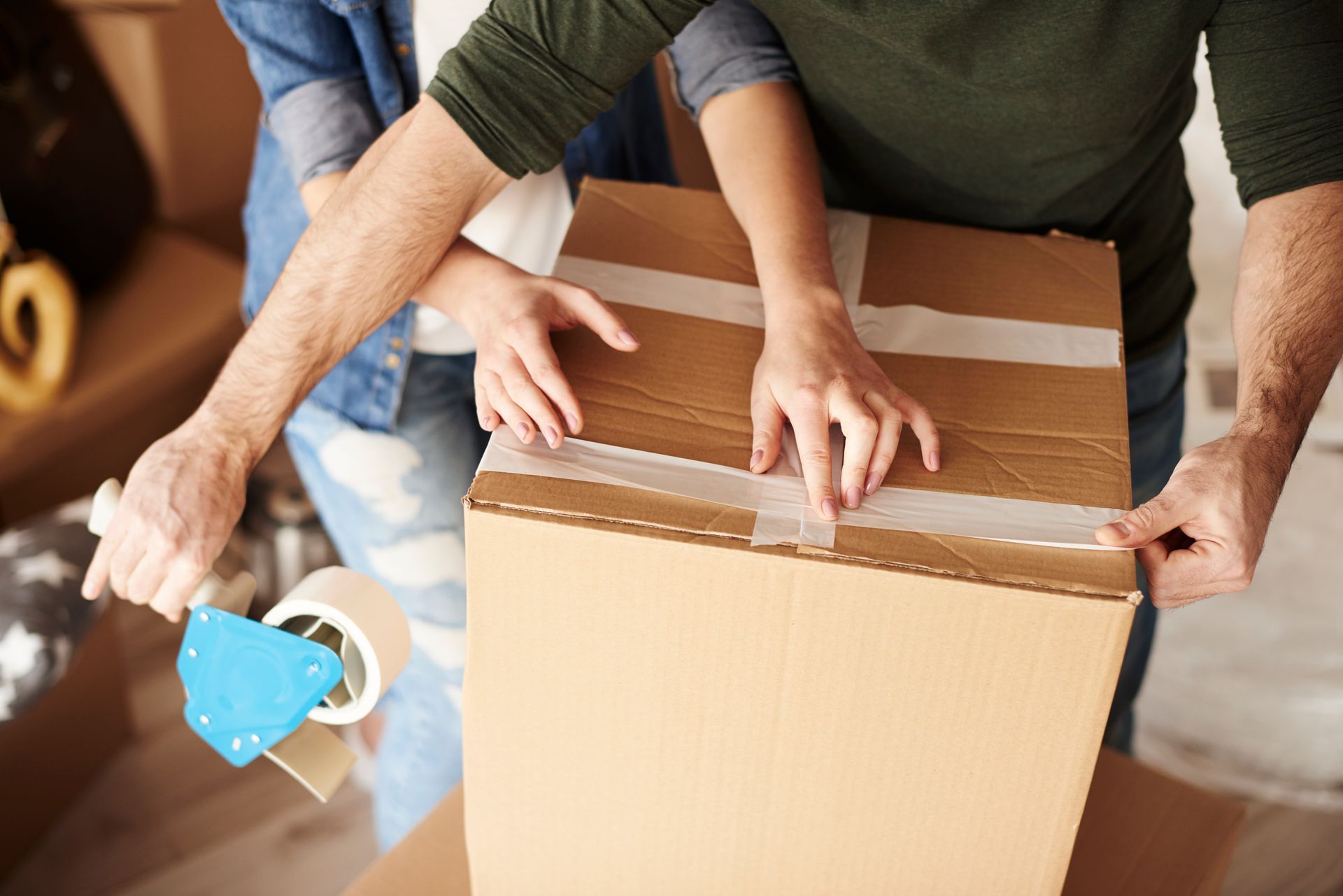 Couple sealing a cardboard box with tape during a move, indoors.