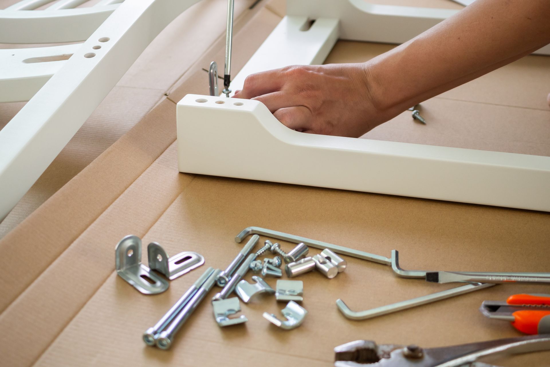 Person assembling white furniture with tools on cardboard.