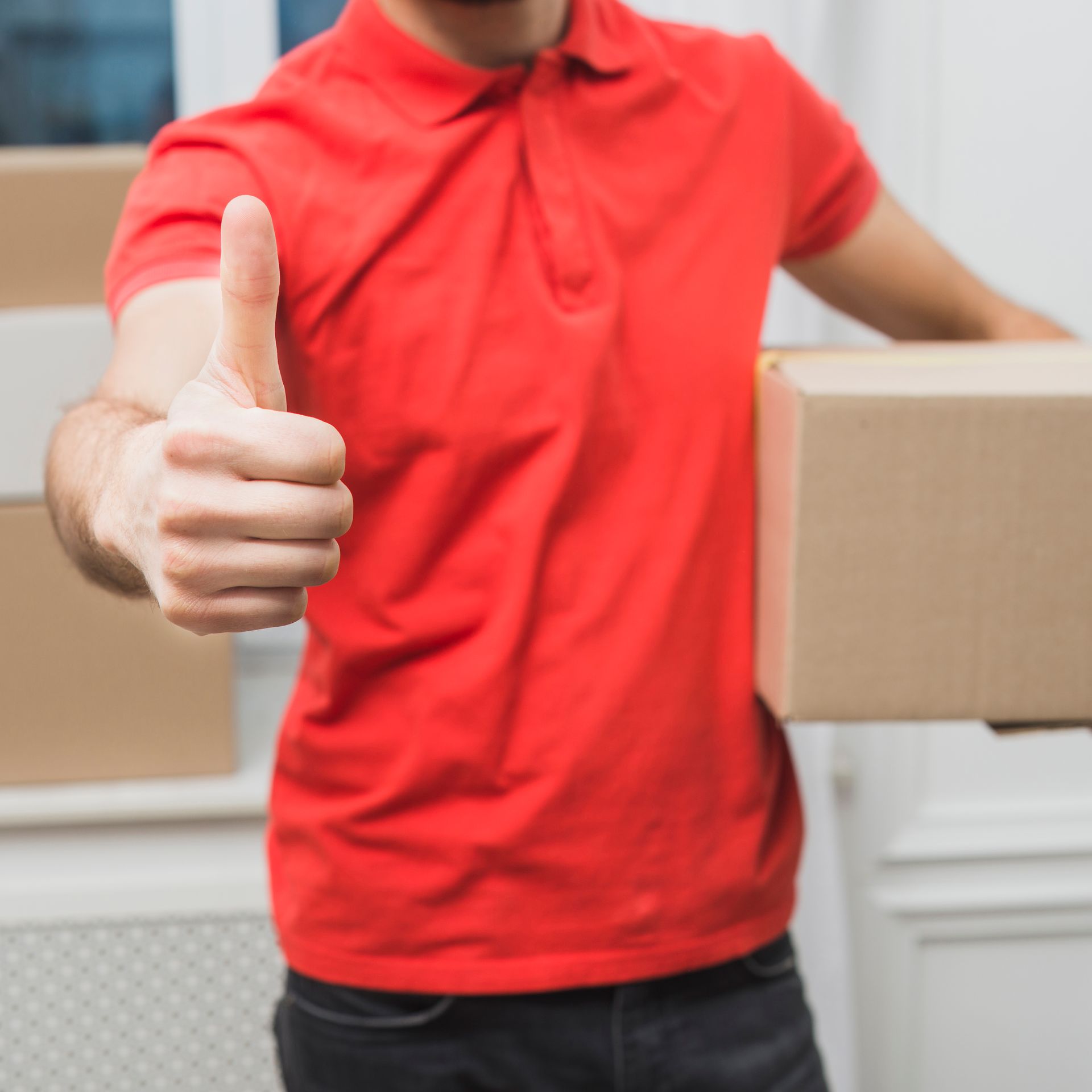 a man in a red shirt is holding a cardboard box and giving a thumbs up