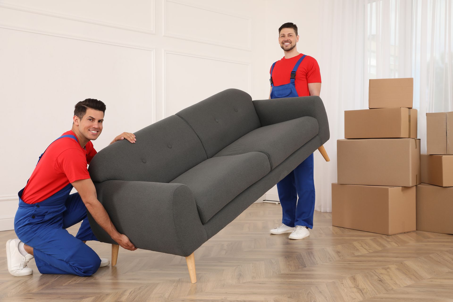 two men are moving a couch in a room filled with cardboard boxes