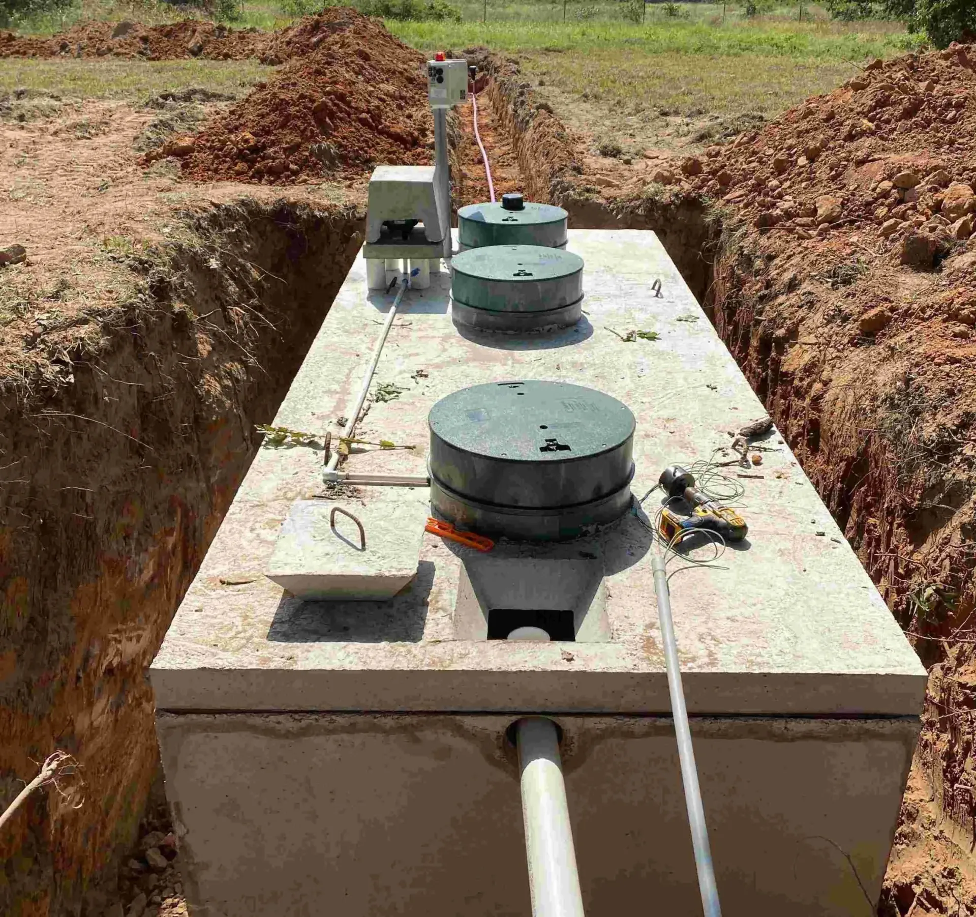 Concrete septic tank in a trench with three green lids and plumbing.