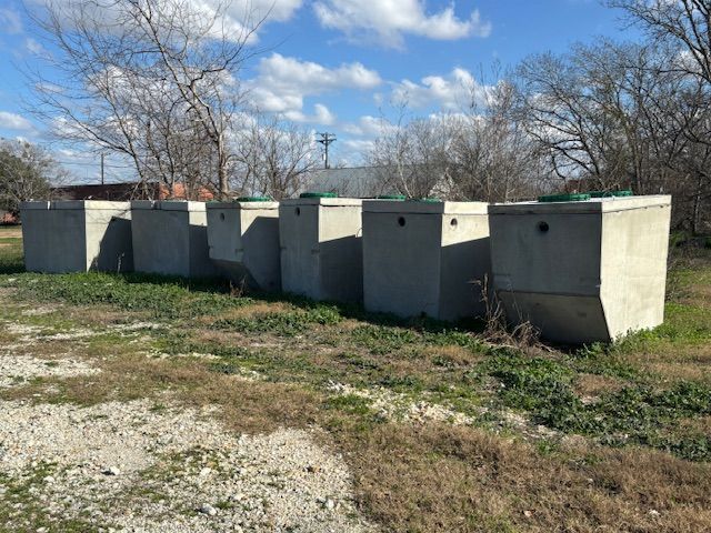 Row of gray concrete septic tanks on a grassy area, under a blue sky with clouds.