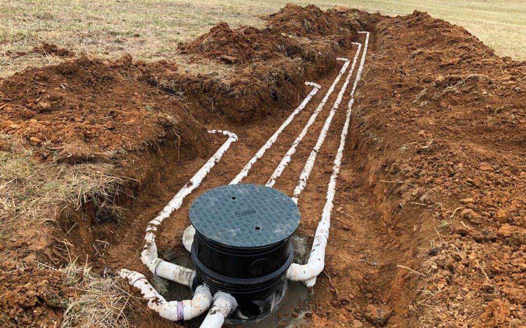 Open septic system with white pipes running from a black tank in a dirt trench.