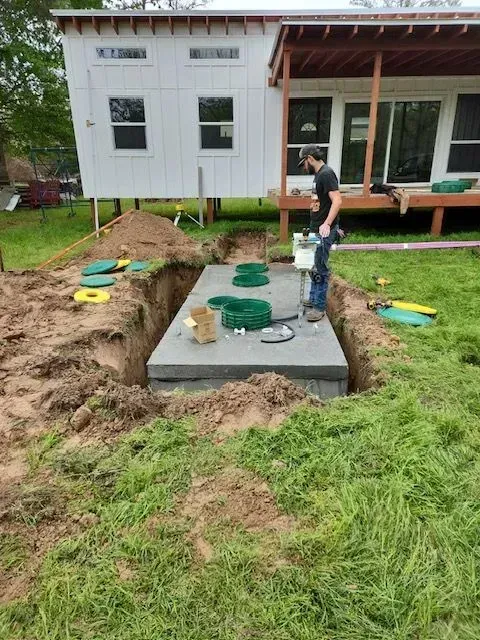 Man installing septic tank in a large dug out pit near a white house.