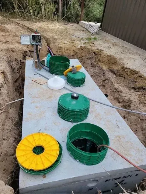 Septic tank installation in progress, with multiple green and yellow access lids open, and equipment nearby.
