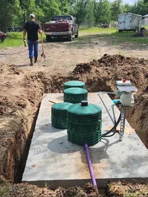 Man walking away from a septic tank installation; green tanks, grey concrete, brown dirt.