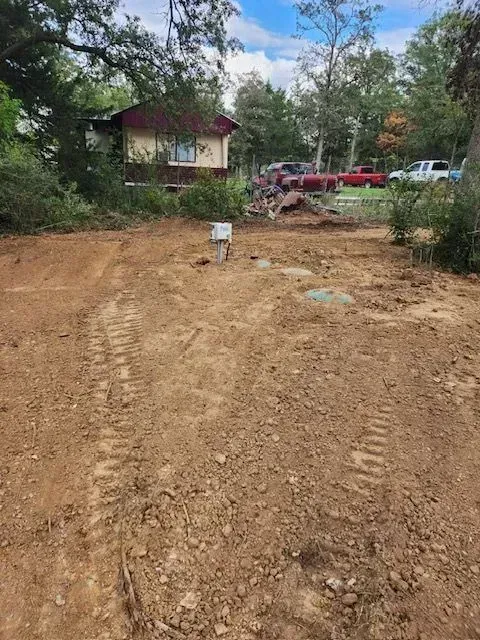 Dirt driveway with tire tracks leading to a house. Several vehicles are parked near the building.