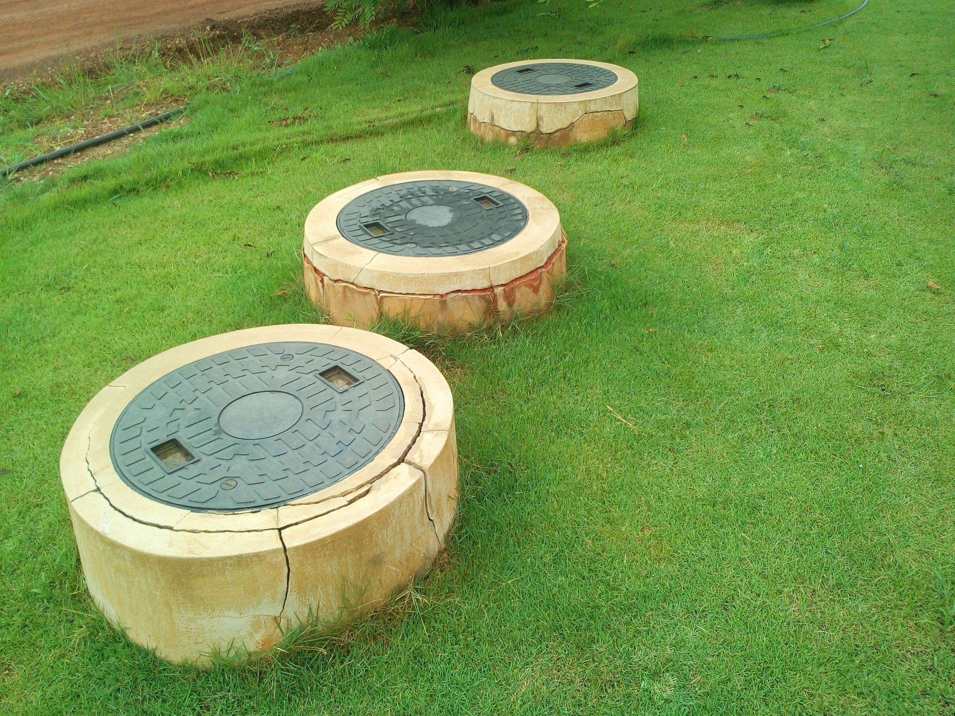 Three concrete septic tank covers with dark lids in a green grassy field.