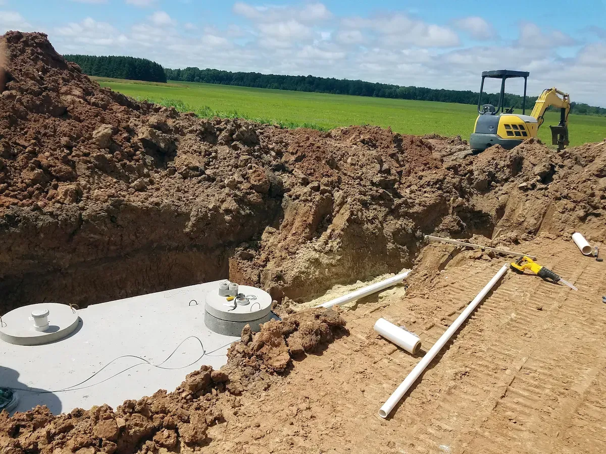 A septic tank installed in a trench at a construction site, with an excavator in the background.