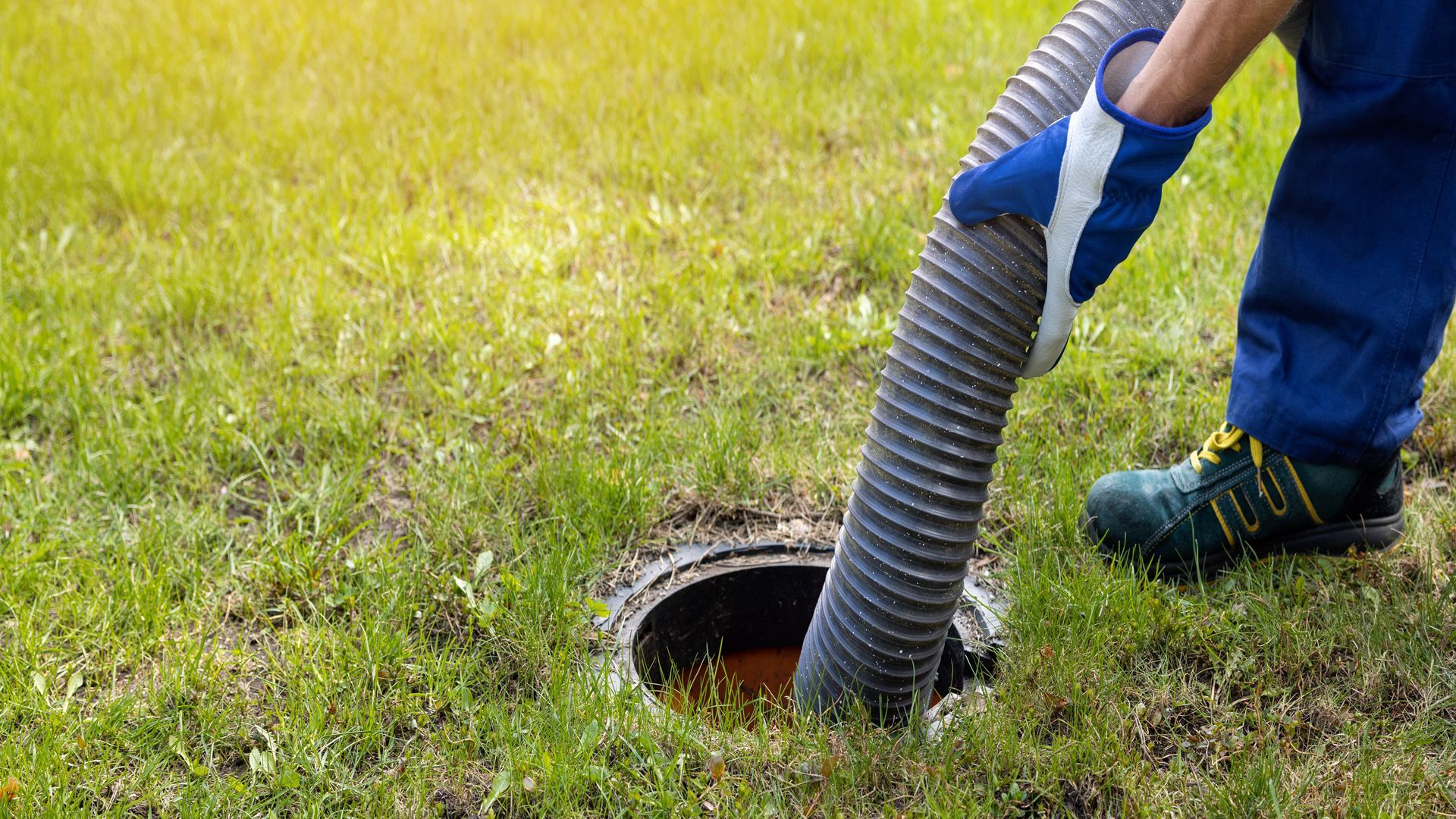 Person wearing gloves and work boots emptying a septic tank with a large hose.