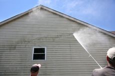 A man is cleaning the side of a house with a high pressure washer.