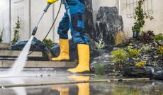 A man in yellow boots is using a high pressure washer to clean a sidewalk.