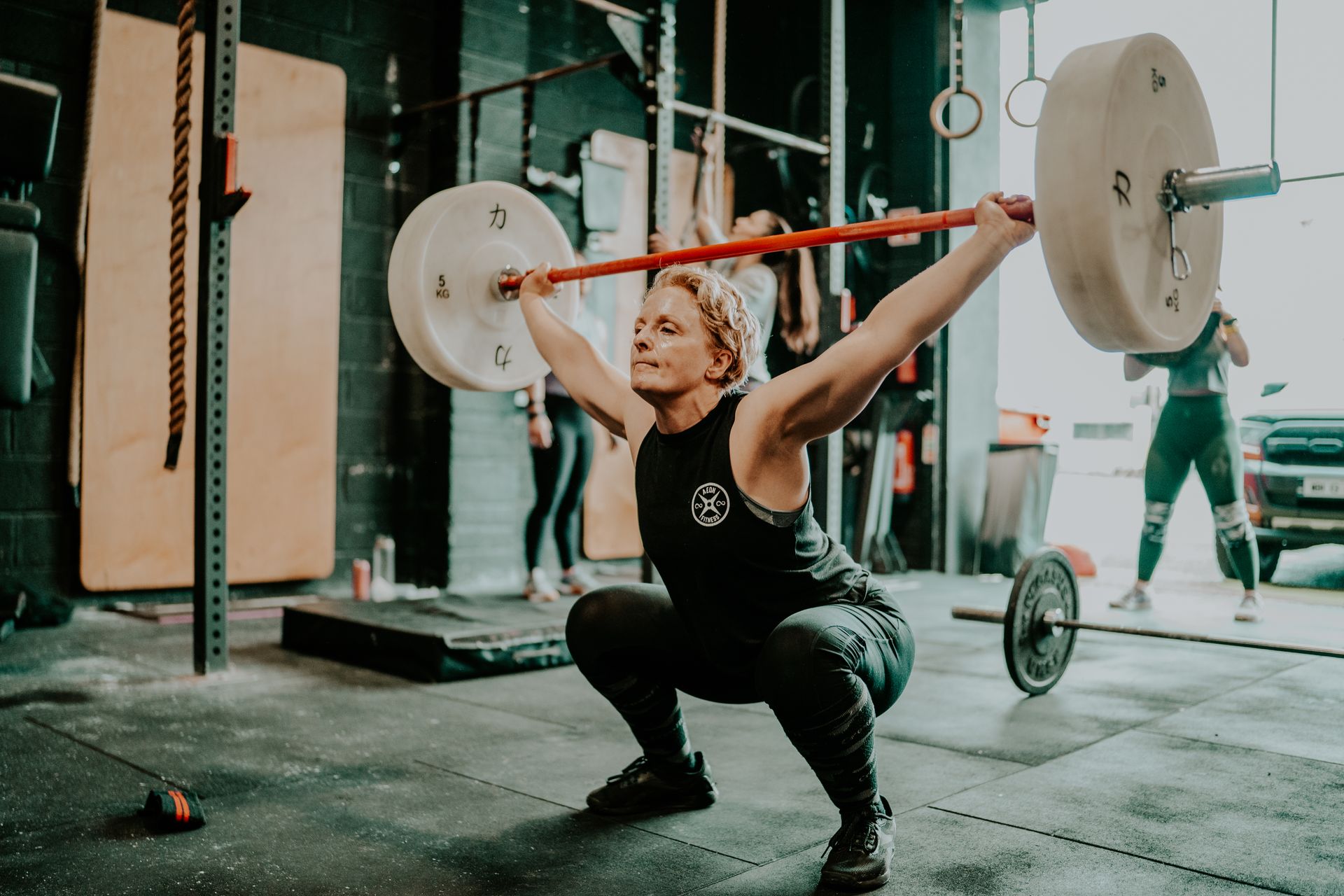A woman is squatting with a barbell over her head in a gym.