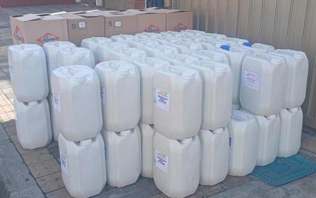 Contenedores de plástico blancos apilados al aire libre. Algunos tienen tapas y etiquetas azules. Cajas de cartón al fondo.