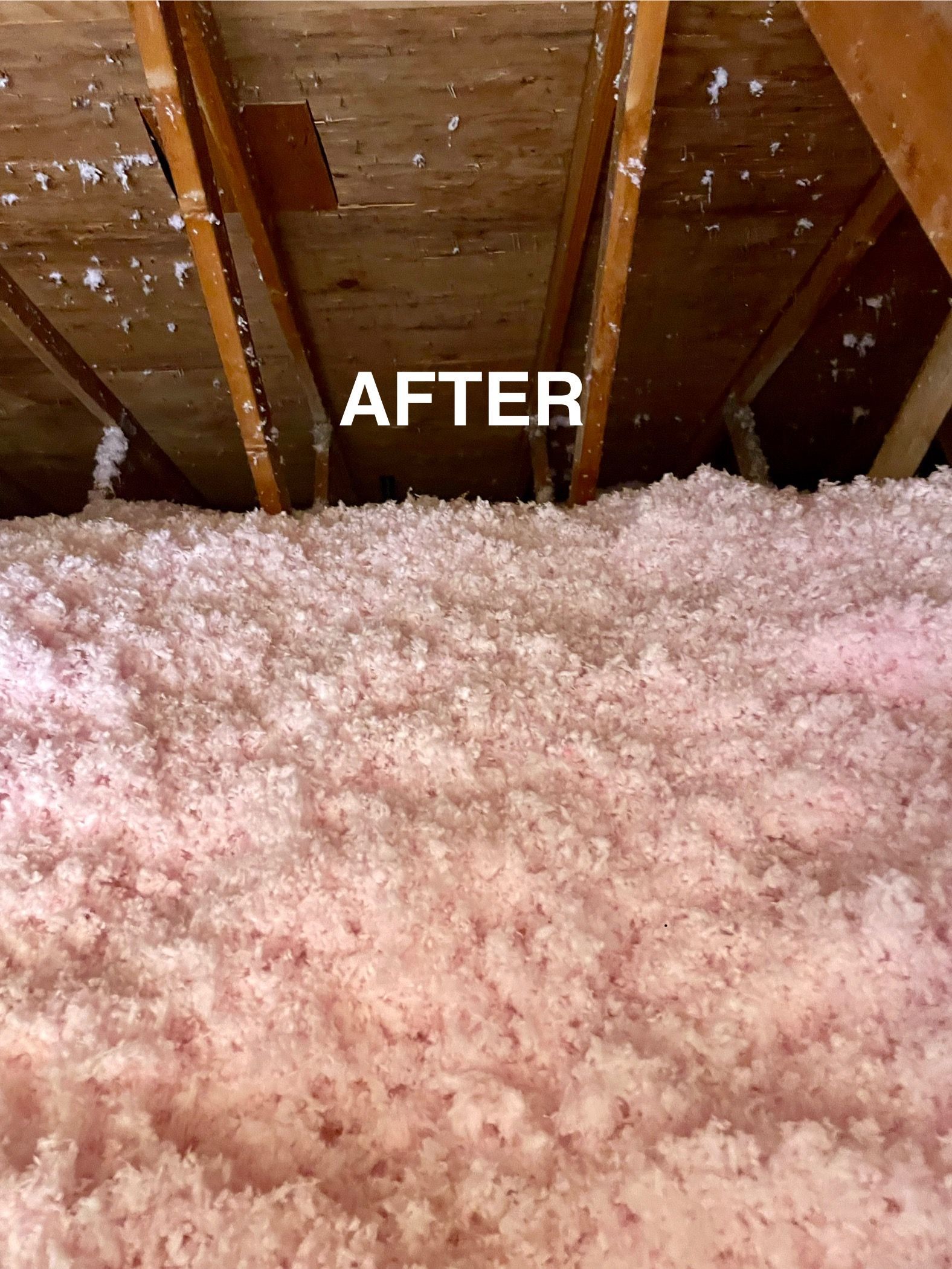 Pink insulation fills an attic space after renovation, with wooden beams above.
