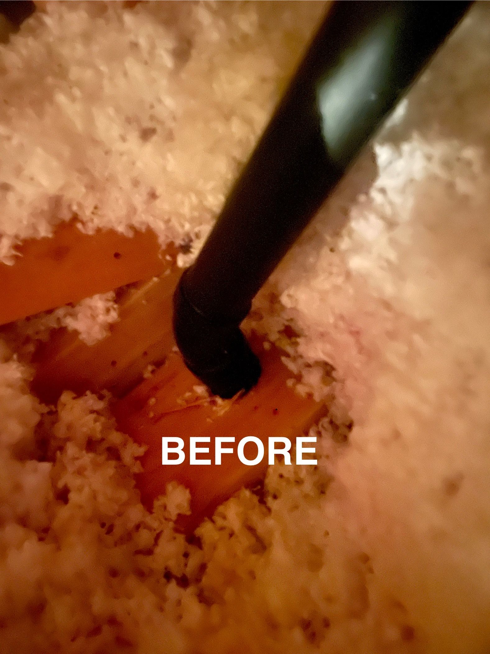 Black pipe entering dusty insulation. Brown wood is visible. 