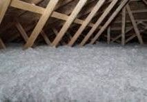 Attic filled with thick, light-colored insulation; sunlight streams through a small window.