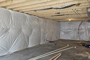 Basement with white insulation on walls, wooden beams overhead, concrete floor, pipes.