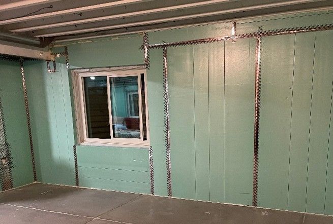 Basement with window and green insulation panels, metal trim. Interior renovation.