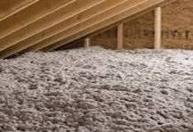 Person in protective suit blowing insulation into an attic.