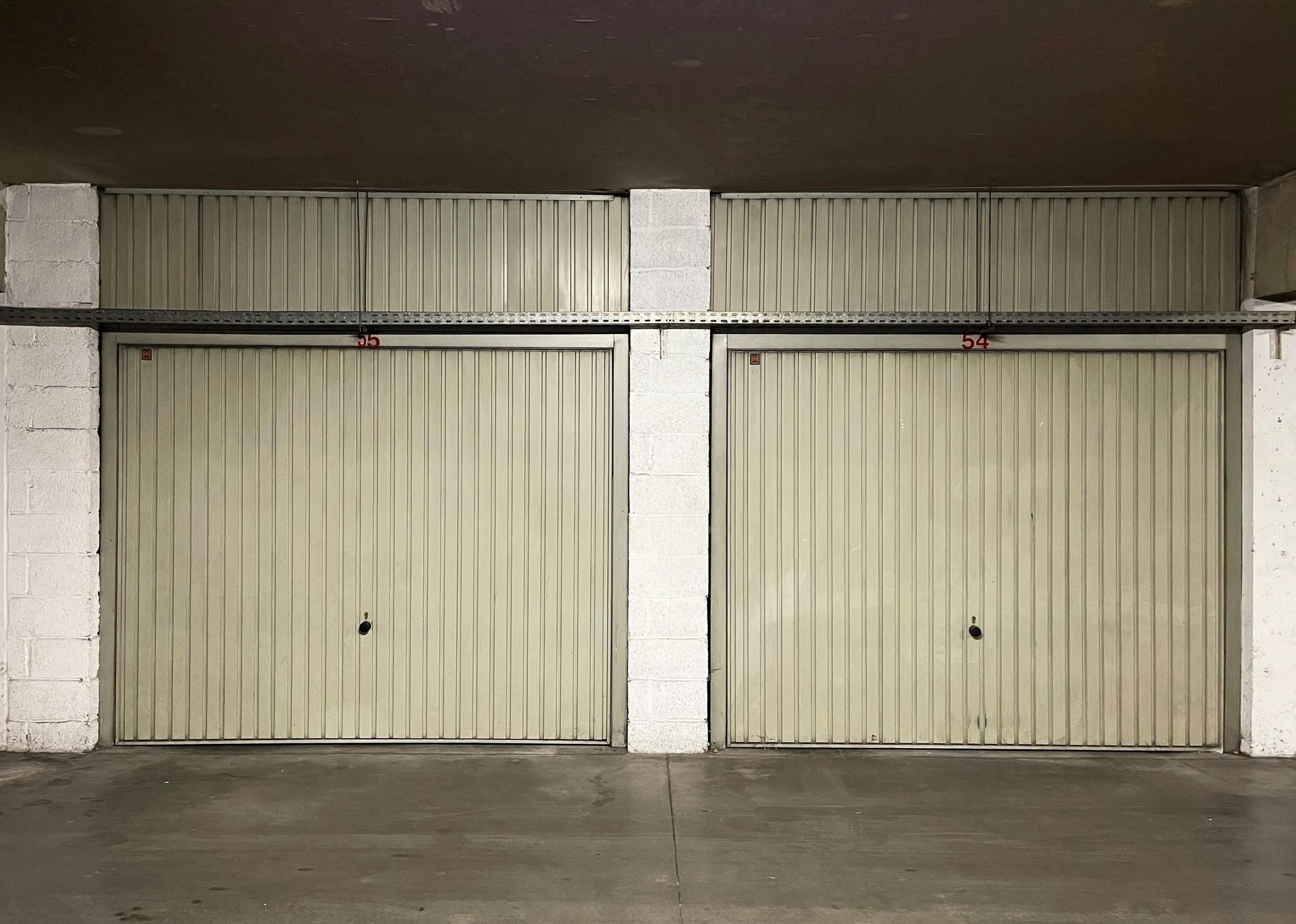 Two beige metal garage doors in an enclosed, concrete space.